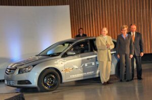 GM CEO with Chevy Volt "mule" during dedication of the automaker's new battery lab. Governor Jennifer Granholm and product engineering chief Jim Queen are to Henderson's left.