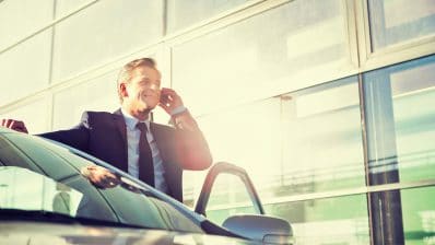 Businessman talking on smartphone while standing outside car