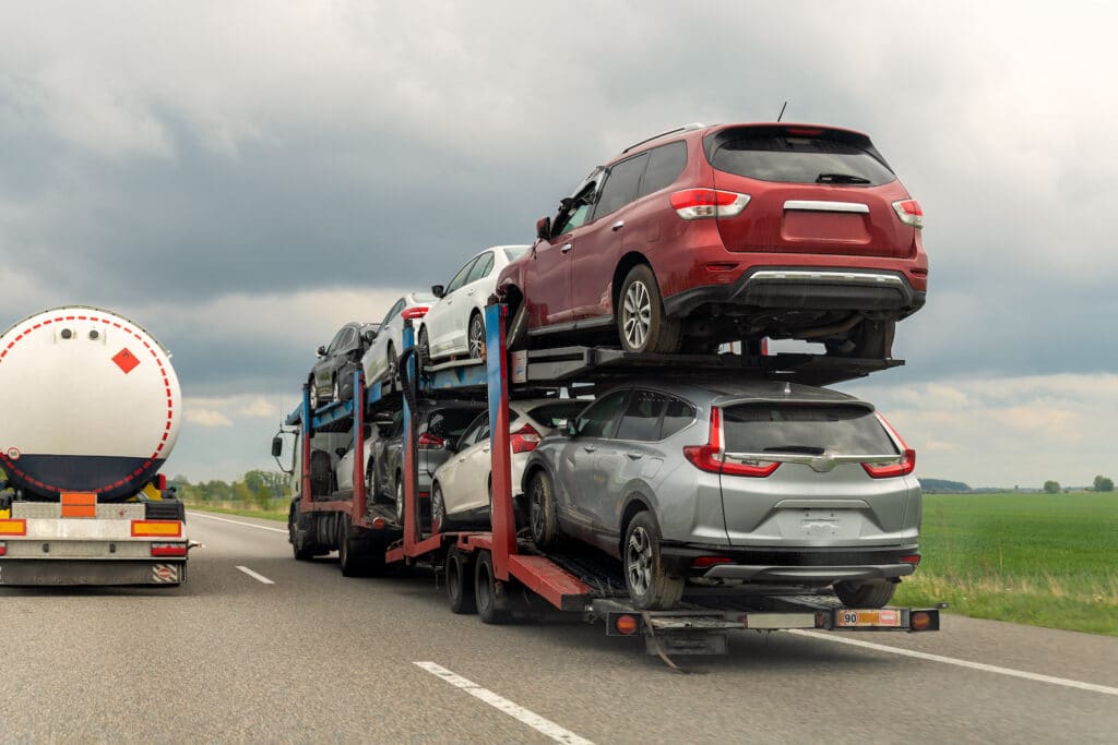 Tow truck car carrier semi trailer on highway carrying batch of damaged cars sold on insurance car auctions for repair and recovery. Vehicles shipment and rescue service
